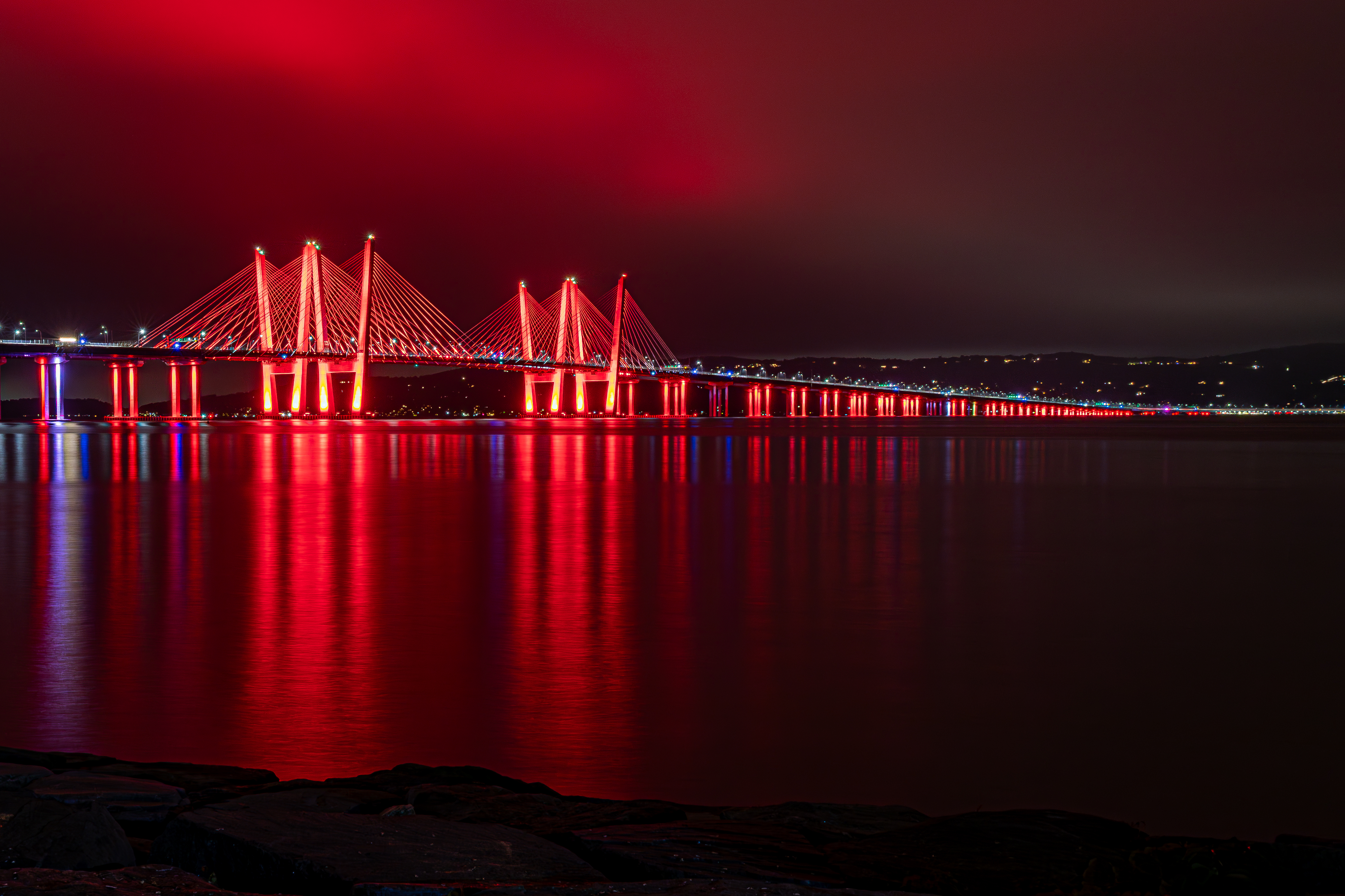 Cable-stayed bridge lit in red at night, reflected in calm water